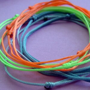 May include: A set of colorful string bracelets in shades of blue, green, and orange. The bracelets are made of thin, braided cords and are tied together in a knot.