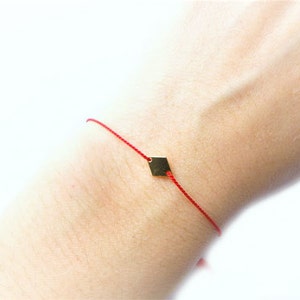 May include: A red string bracelet with a small gold diamond charm.