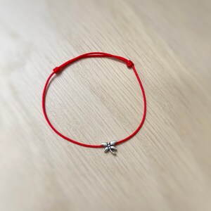 May include: A red string bracelet with a silver dragonfly charm.