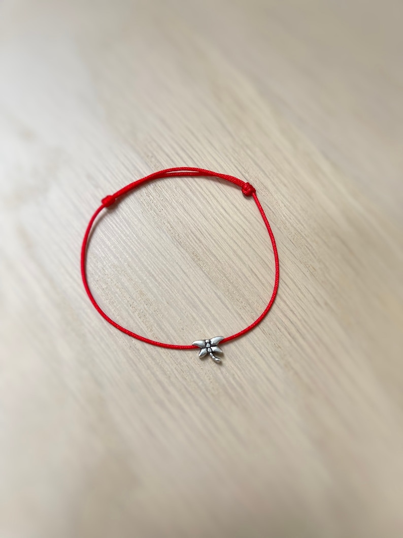 May include: A red string bracelet with a silver dragonfly charm.