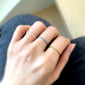 Peut inclure: Gros plan sur trois bagues minimalistes, blanches, turquoise et vertes. Les anneaux fins sont portés aux doigts. Les bagues semblent être faites d'un fil fin, sur un fond flou.