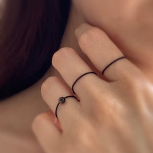 Może przedstawiać: Ręka z trzema cienkimi czarnymi gumowymi pierścionkami na trzech r&oacute;żnych palcach.