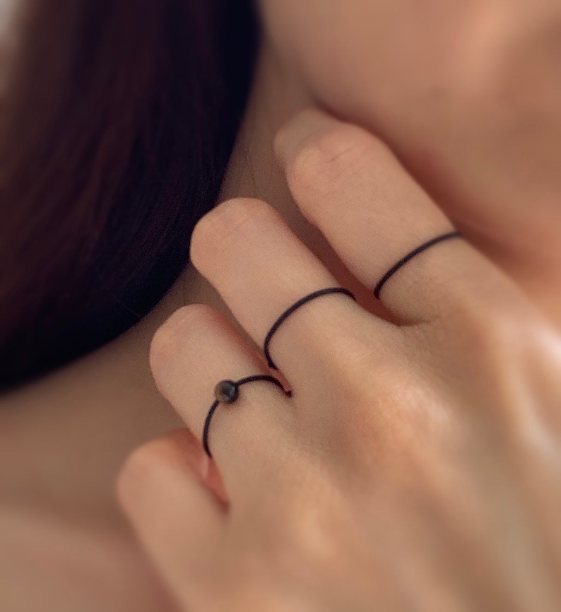 Może przedstawiać: Ręka z trzema cienkimi czarnymi gumowymi pierścionkami na trzech r&oacute;żnych palcach.