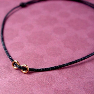 Könnte beinhalten: Eine schwarze Schnurkette mit einem goldenen Unendlichkeits-Anhänger.