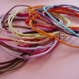 Pode incluir: Uma coleção de pulseiras de amizade coloridas feitas de cordões finos amarrados juntos em uma variedade de nós. As pulseiras são em tons de vermelho, laranja, amarelo, verde, azul, roxo e marrom.