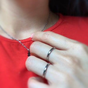May include: A person wearing two thin silver rings on their finger. The rings are simple and elegant.