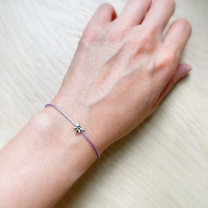 May include: A delicate purple cord bracelet with a small silver dragonfly charm.