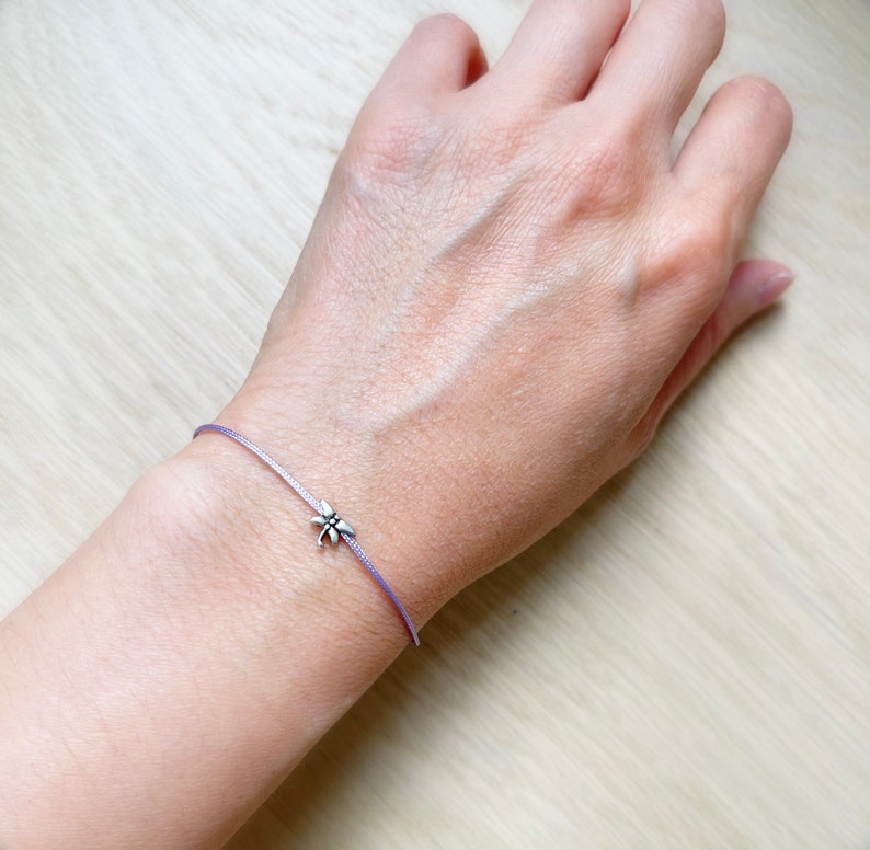 May include: A delicate purple cord bracelet with a small silver dragonfly charm.