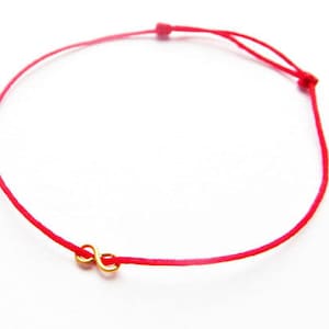 May include: A red string bracelet with a gold infinity symbol charm.