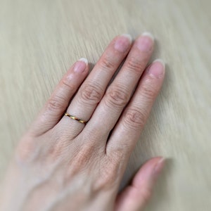 Może przedstawiać: Zbliżenie na dłoń z cienkim, plecionym pierścionkiem z ż&oacute;łtych, pomarańczowych i brązowych nici.