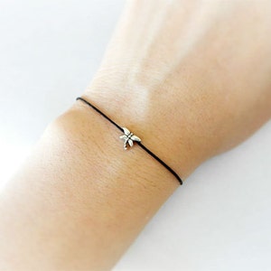 May include: A simple black string bracelet with a silver dragonfly charm.