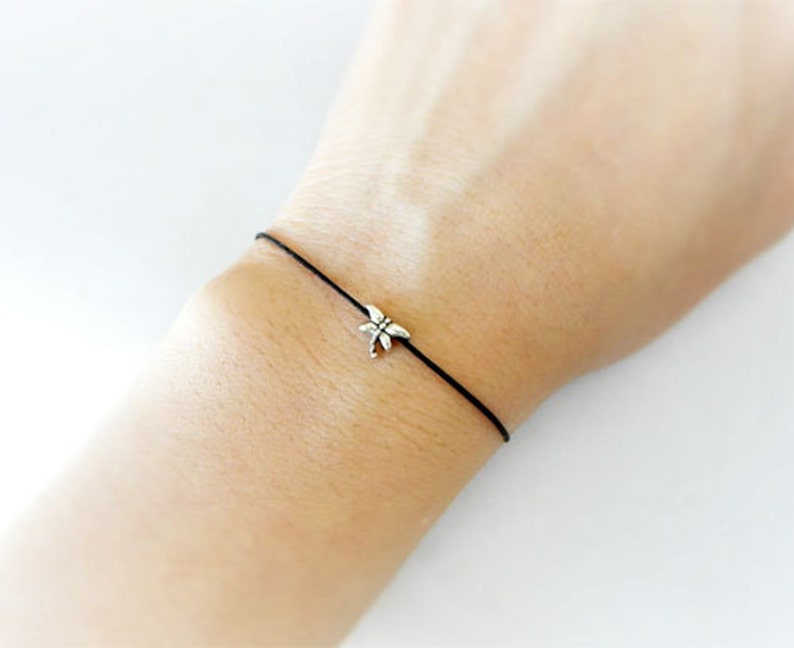 May include: A simple black string bracelet with a silver dragonfly charm.