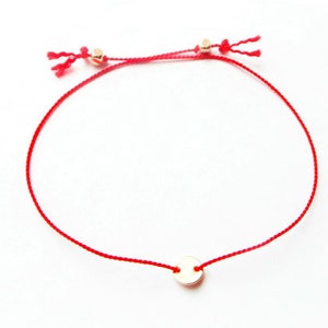 May include: A red string bracelet with a small gold circle charm.
