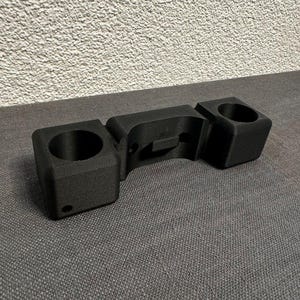 Könnte beinhalten: Ein schwarzer 3D-gedruckter Telefonständer mit zwei Getränkehaltern. Der Ständer ist so konzipiert, dass er ein Telefon und zwei Becher aufnehmen kann.