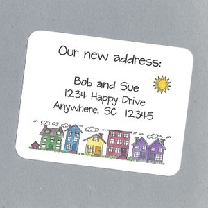 May include: A white card with a handwritten message that says "Our new address: Bob and Sue 1234 Happy Drive Anywhere, SC 12345". A small sun is drawn in the upper right corner. A row of colorful houses is drawn at the bottom of the card.