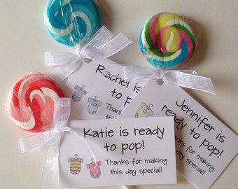 May include: Three lollipop favors with white ribbon bows and attached tags. The tags have the text "Rachel is to F", "Jennifer is ready to pop!" and "Katie is ready to pop! Thanks for making this day special!" The lollipops are red and white, blue and white, and green, yellow, and blue.