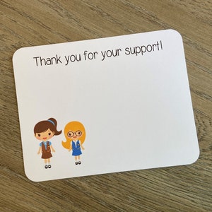 May include: White rectangular card with rounded corners, featuring the text "Thank you for your support!" above two cartoon figures. One figure has brown hair and the other has blonde hair and glasses. The figures are wearing blue and brown uniforms.