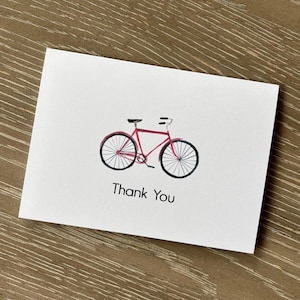 May include: A white greeting card with a red bicycle illustration. The bicycle has black tires and a black seat. The words "Thank You" are printed in black below the bicycle.