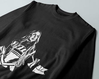 May include: Black sweatshirt with a white graphic print of a woman with long hair. The woman is wearing a white and black striped shirt.