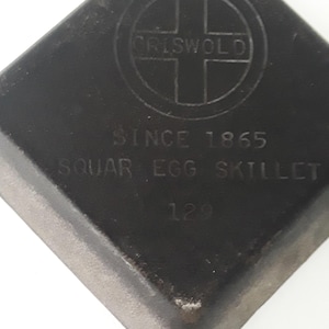 以下が含まれることがあります： 黒い正方形の鋳鉄製グリズウォルドエッグスキレット。 スキレットにはハンドルがあり、円の中に「CRISWOLD」、 「SINCE 1865」、「SQUAR EGG SKILLET」、および「129」というテキストが表示されています。