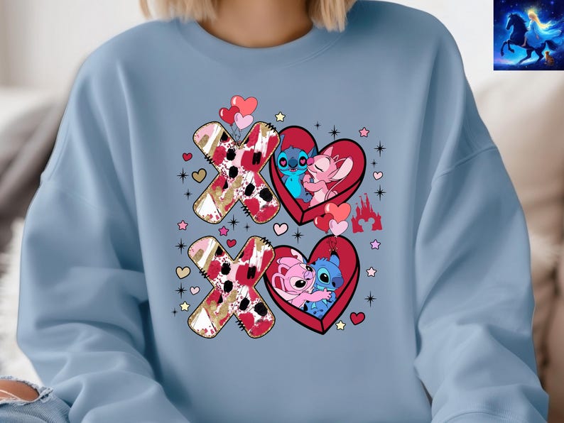K&ouml;nnte beinhalten: Hellblaues Sweatshirt mit einem Valentinstagsdesign. Das Design zeigt die Buchstaben X und O, Herzen und die Zeichentrickfiguren Stitch und Angel. Die X und O haben ein rotes, goldenes und wei&szlig;es Muster.