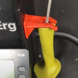 May include: A red plastic hook attached to a yellow rubber handle with a white string. The hook is attached to a black device with the text "Erg" and "PM6" visible.