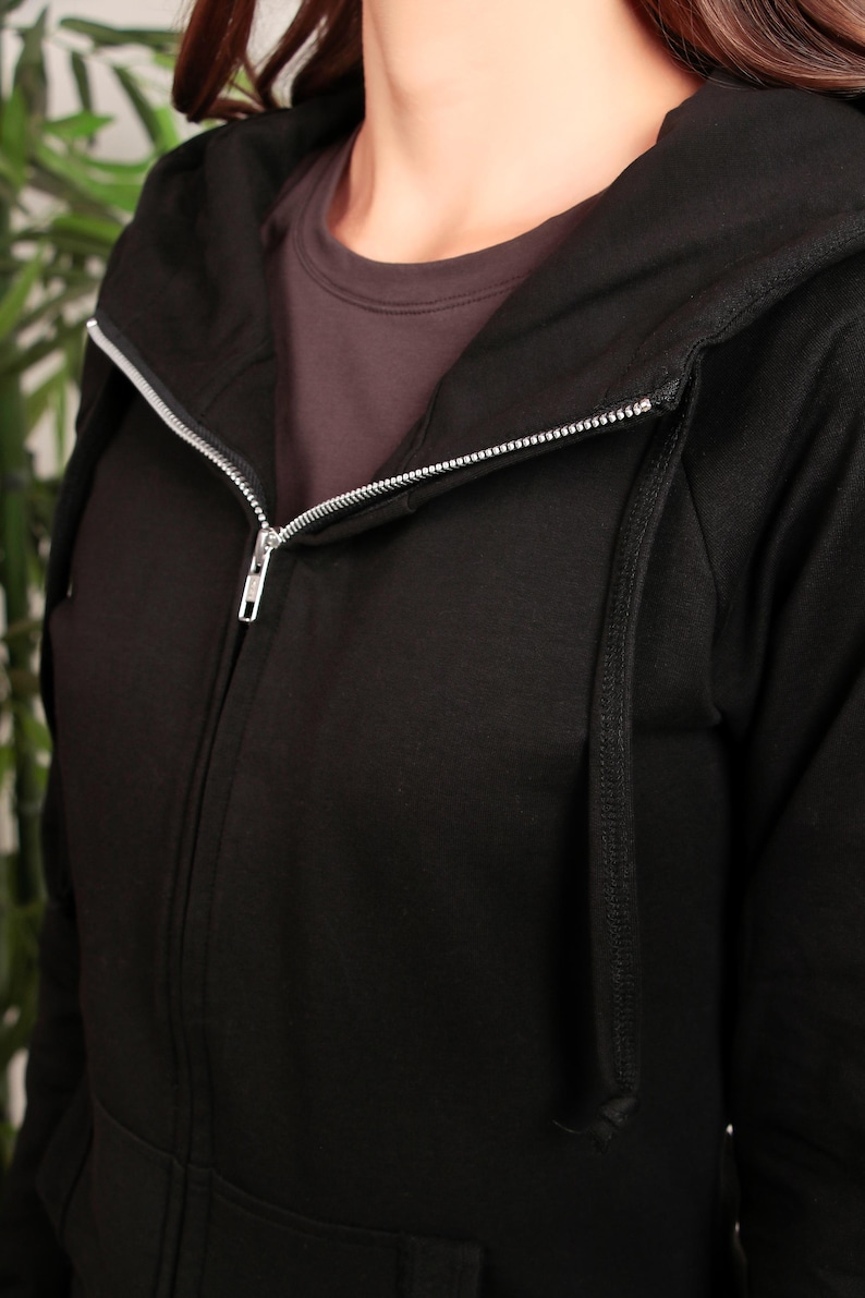 Puede incluir: Sudadera con capucha negra con cremallera y cord&oacute;n. La cremallera est&aacute; parcialmente abierta, revelando una camiseta interior gris.