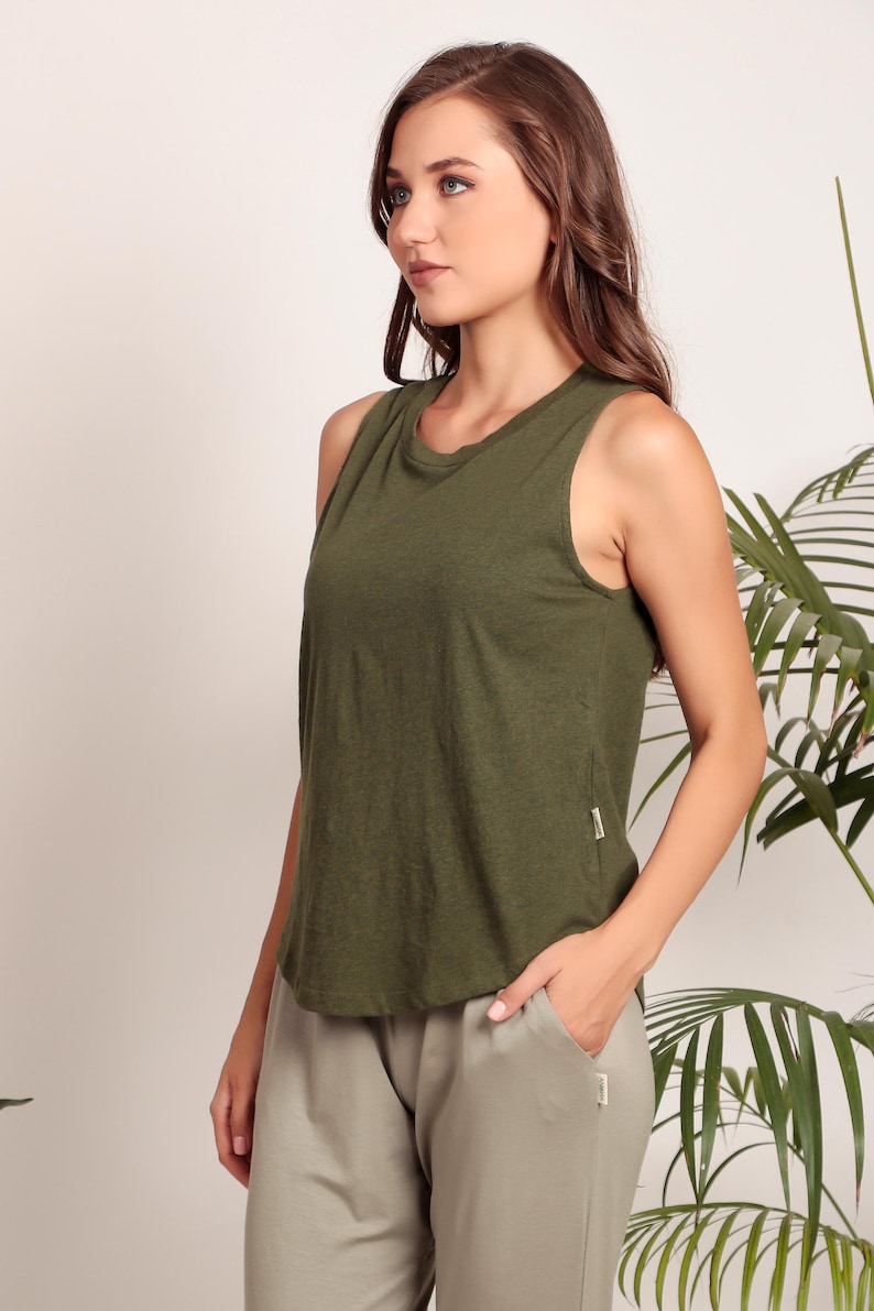 May include: A woman wearing a green sleeveless shirt and light gray pants. The shirt is made of a soft, comfortable fabric and has a relaxed fit.