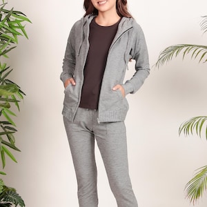 Puede incluir: Una sudadera con capucha gris y pantalones deportivos a juego. La sudadera tiene una cremallera y una capucha con cord&oacute;n. Los pantalones deportivos tienen una cintura con cord&oacute;n y bolsillos.
