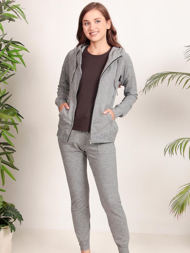 Puede incluir: Una sudadera con capucha gris y pantalones deportivos a juego. La sudadera tiene una cremallera y una capucha con cord&oacute;n. Los pantalones deportivos tienen una cintura con cord&oacute;n y bolsillos.
