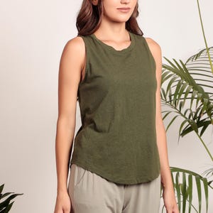 May include: A woman wearing a green sleeveless tank top and beige pants. The tank top has a round neckline and a relaxed fit.