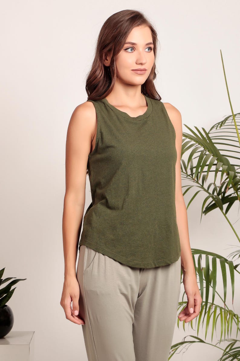 May include: A woman wearing a green sleeveless tank top and beige pants. The tank top has a round neckline and a relaxed fit.