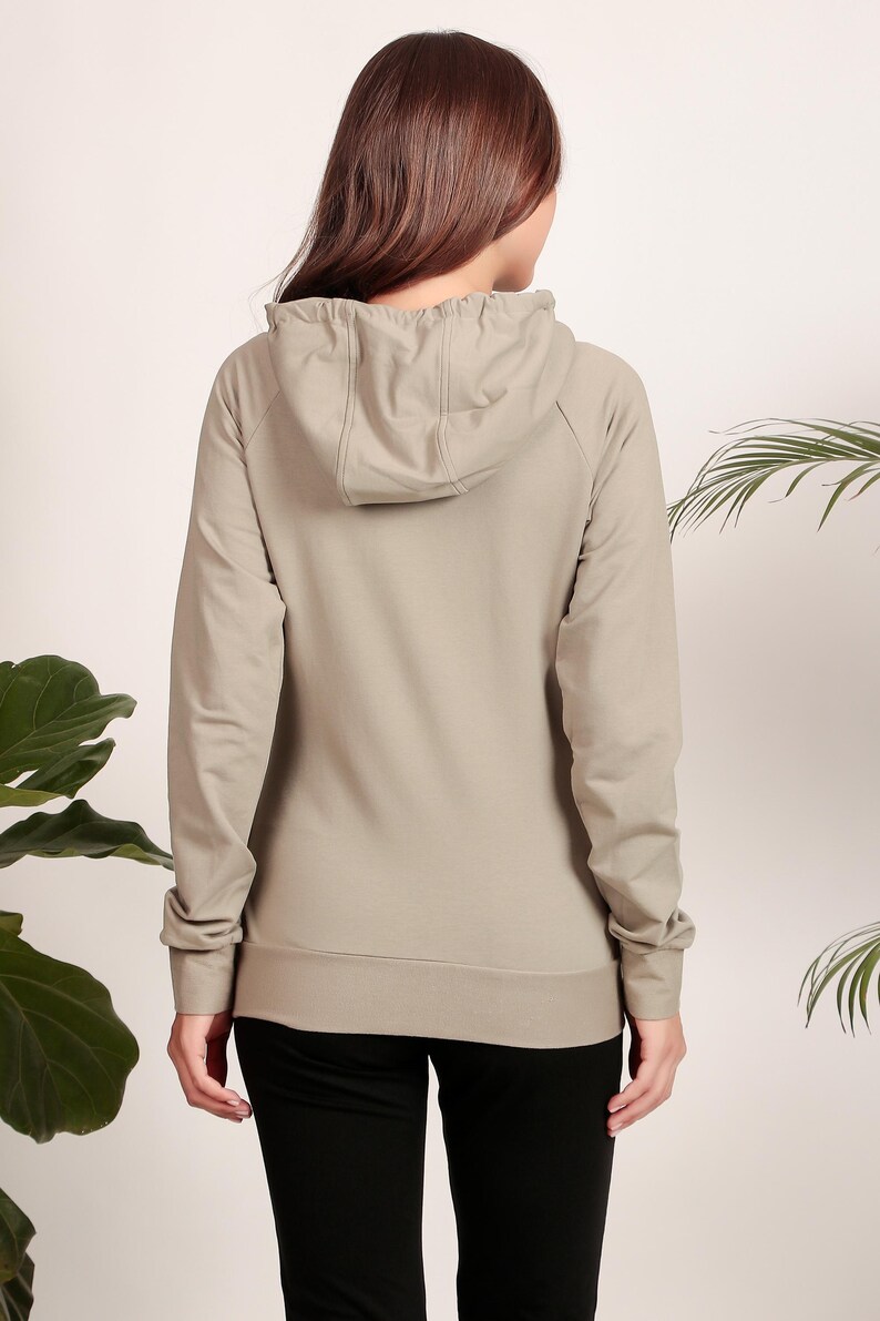 Puede incluir: Una sudadera con capucha de color gris claro con cord&oacute;n de ajuste. La sudadera tiene un corte holgado y mangas largas.