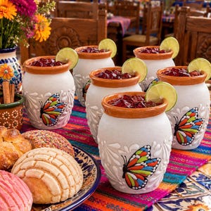 May include: Five white ceramic clay cups with terracotta rims, each featuring a hand-painted monarch butterfly and embossed leaf patterns. Each cup is filled with a dark red beverage and garnished with a fresh green lime slice.