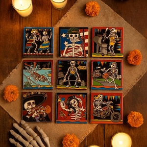 May include: Nine square ceramic tiles with Day of the Dead skeleton designs. Each tile features a unique skeleton scene, including dancing, weightlifting, and playing musical instruments. The tiles are set on a burlap surface with orange flowers and candles.