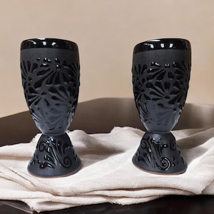 Peut inclure: Deux gobelets en céramique noire avec des motifs floraux complexes. Les gobelets ont une base large et un bol arrondi.