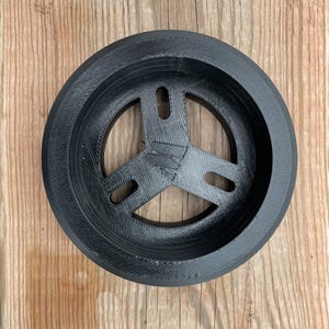 May include: A black plastic 3D printed ring with a three-pronged design in the center. The ring has a raised outer edge.