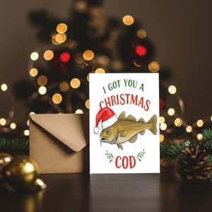 May include: A festive Christmas card featuring a cod wearing a Santa hat, with the text "I GOT YOU A CHRISTMAS COD". A brown envelope and Christmas tree lights are in the background.