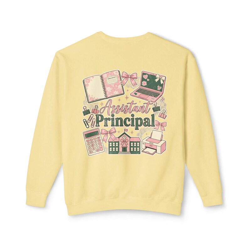 May include: Pale yellow sweatshirt with a colorful graphic design. The design includes a notebook, laptop, calculator, printer, schoolhouse, and bows. The words "Assistant Principal" are in the center of the design.