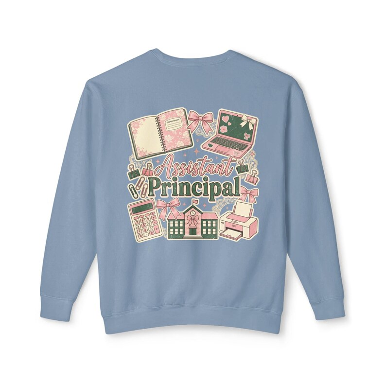 May include: A light blue sweatshirt with a graphic design featuring school-related items such as a laptop, calculator, and notebook. The words "Assistant Principal" are in the center of the design.