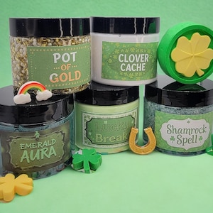 May include: A collection of jars with black lids, each labeled with St. Patrick's Day themed names like "Pot of Gold" and "Shamrock Spell." The jars are filled with colorful contents and surrounded by decorative charms, including a rainbow, shamrocks, and a horseshoe.