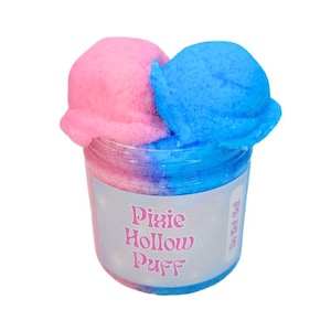 May include: A clear plastic jar filled with pink and blue fluffy material. The jar has a label that reads "Pixie Hollow Puff". The fluffy material is a vibrant pink and blue color.