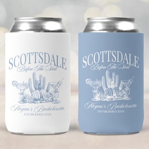 May include: Two white and blue can coolers with a cactus and margarita design. The text on the coolers reads "Scottsdale Before The Veil" and "Megan's Bachelorette Established 2024".