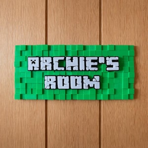 May include: A green pixelated sign with the text "ARCHIE'S ROOM" in white block letters. The sign is mounted on a wooden door. The sign has a pixelated design, reminiscent of a video game.