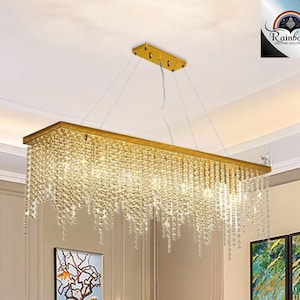 May include: A gold rectangular chandelier with crystal strands hanging down. The chandelier is suspended from the ceiling by multiple wires.