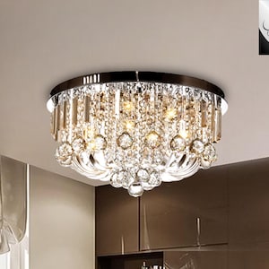 May include: A modern chrome and crystal flush mount ceiling light fixture with a round shape. The light fixture has multiple crystal strands and clear glass bulbs.