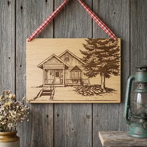 May include: Wooden sign featuring an etched illustration of a house and a tree. The sign is suspended by a red and white checkered ribbon. The artwork is displayed against a weathered wooden wall, evoking a rustic aesthetic.