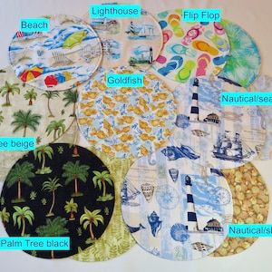 May include: Ten round fabric placemats with various beach-themed designs. The designs include palm trees, lighthouses, seashells, fish, and flip flops. The placemats are in various colors, including beige, black, blue, and white.