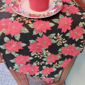 May include: Black table runner with a red poinsettia and green leaf pattern.