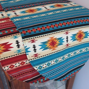 May include: A turquoise, red, and white table runner with a Southwestern geometric pattern. The runner is made of fabric and has a fringed edge.